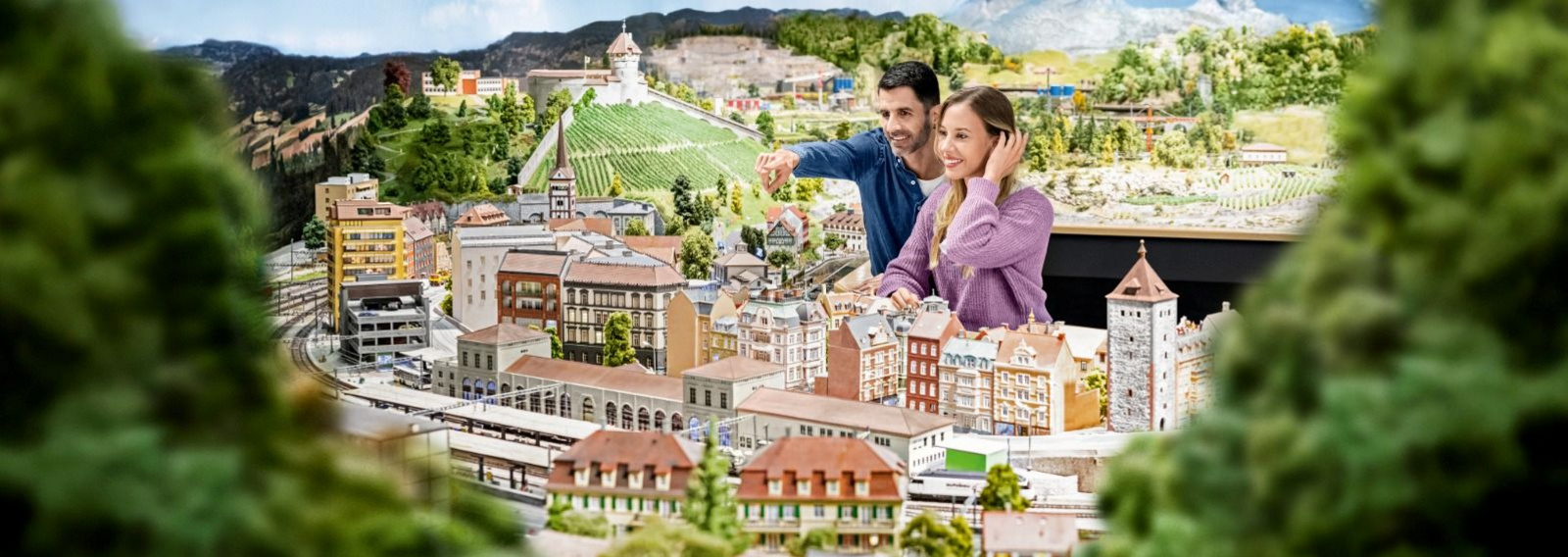 Ein paar steht vor einer Miniaturwelt und bestaunt die Landschaft.