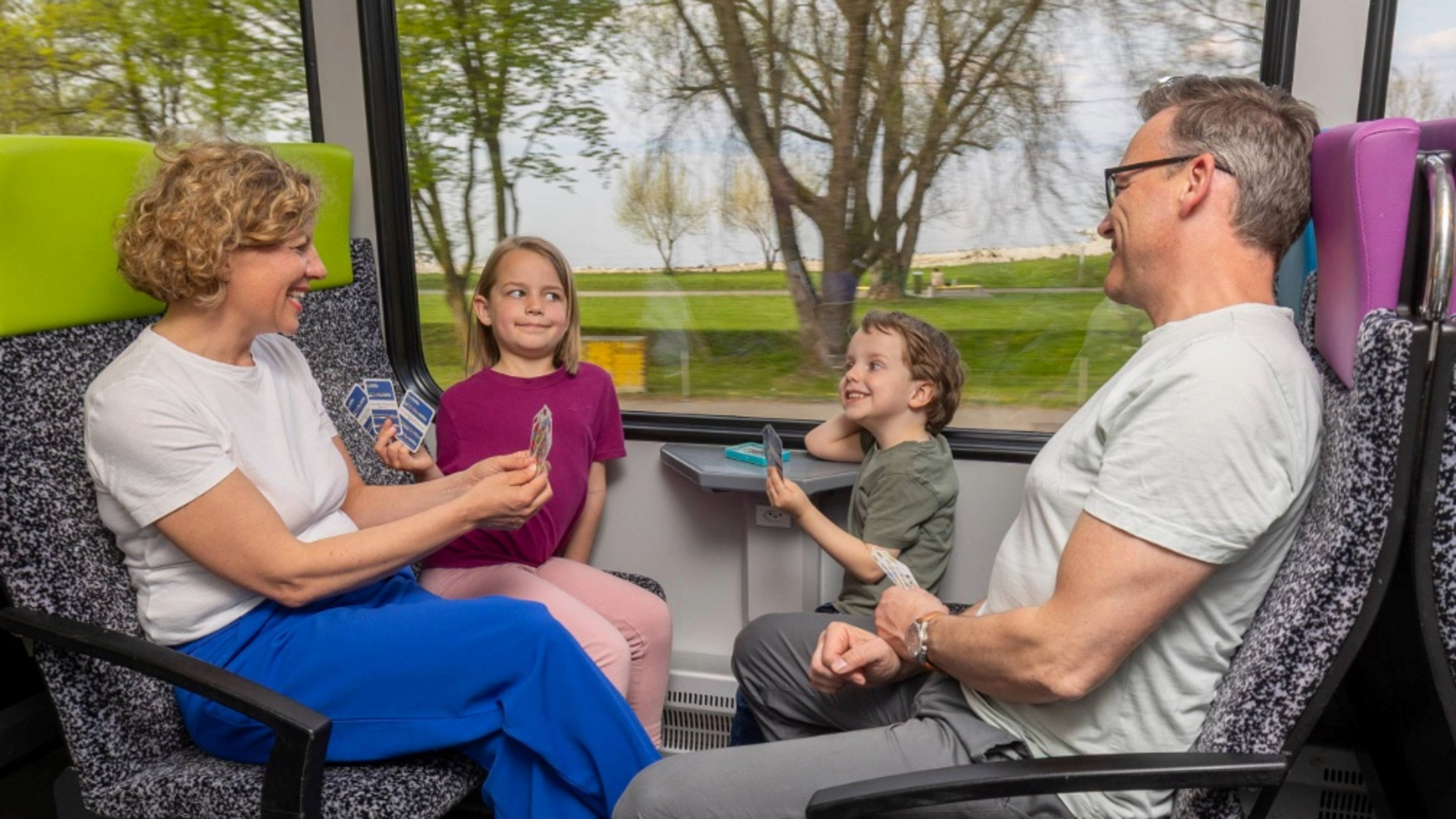 Familie reist zufrieden mit den Kindern im Thurbo Zug, sie spielen ein Kartenspiel.