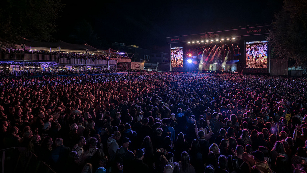 Menschenmenge nachts vor einer Bühne an einem Konzert.