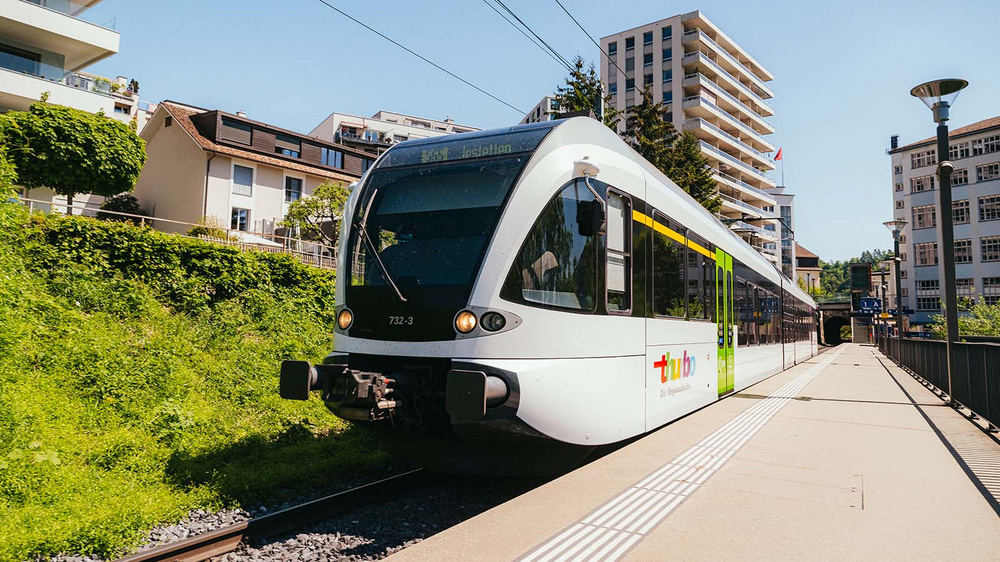 Thurbo Zug an einem Bahnhof mit Häuser im Hintergrund.