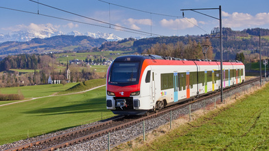 Ein Flirt Evo von Thurbo fährt durch die Frühlingslandschaft. Im Hintergrund sind die Churfirsten zu sehen.