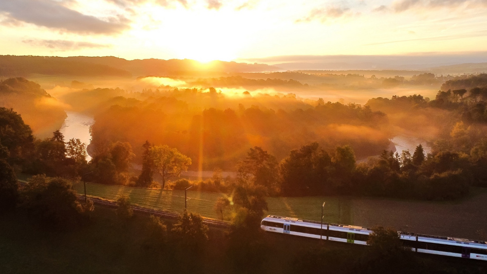 Ein GTW von Thurbo fahrt durch die Landschaft, während die Sonne untergeht.