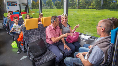 viele Reisende in einem farbigen Zug mit schöner Aussicht in die grüne Landschaft.