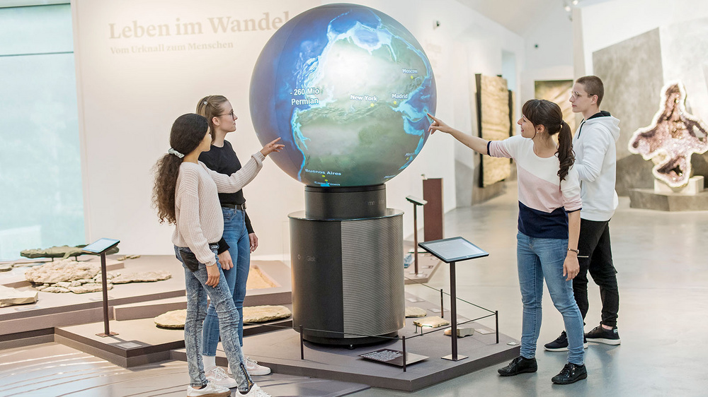 Kinder stehen vor einem grossen Weltatlas in einem Museum.