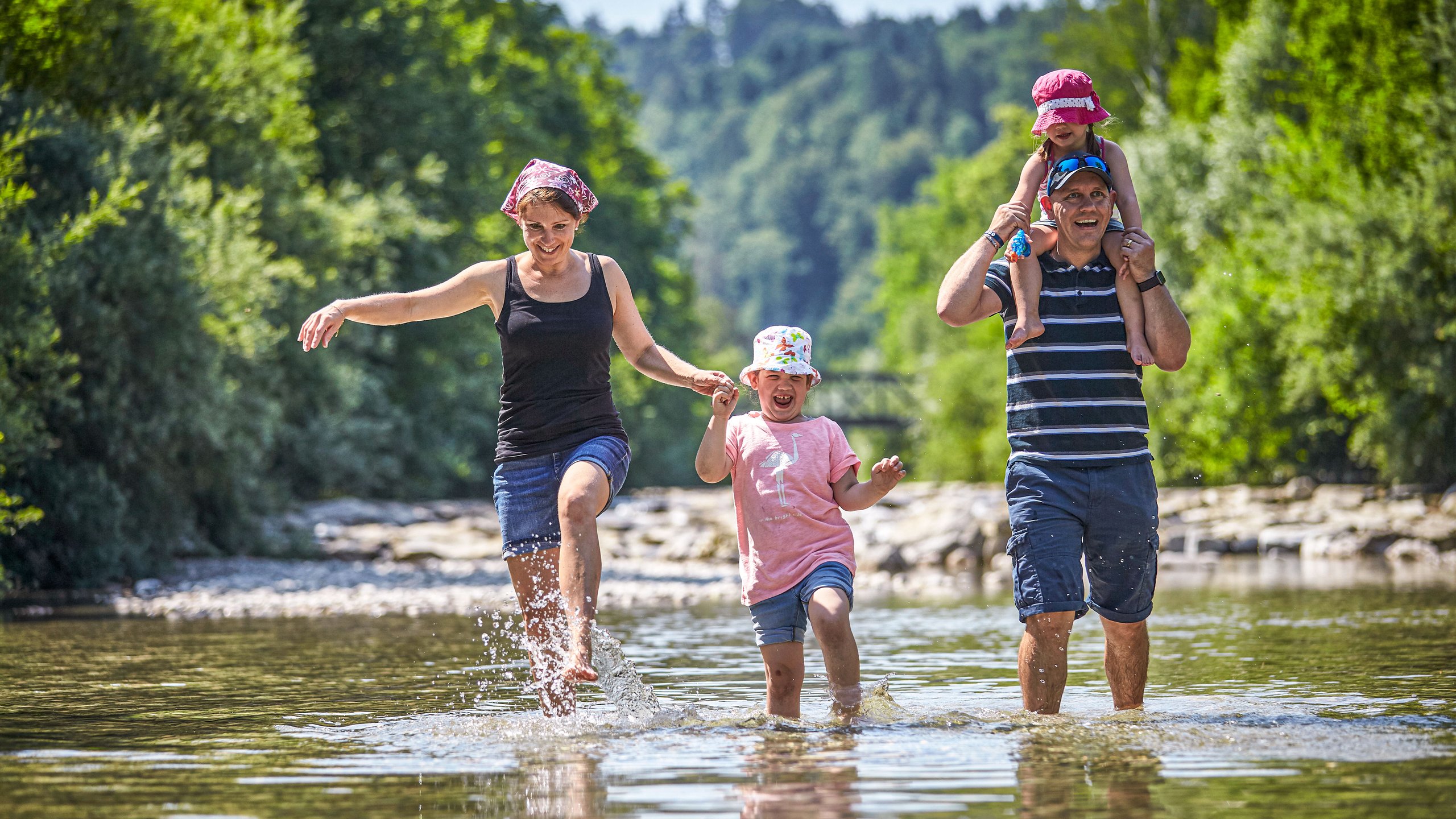 Eine Familie watet fröhlich lachend in einem kniehohen Fluss.